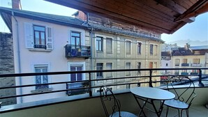 A balcony with a table and chairs, overlooking a row of buildings with balconies and shutters.