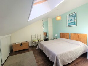Un dormitorio con techo inclinado, una cama con cabecera de madera, una mesita de noche, una silla, un aparador y una lámpara de pared.