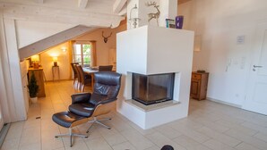 A modern living room with a fireplace, leather chair, dining area, and a view of the outdoors.