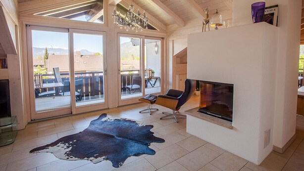 A spacious living room with a fireplace, large sliding glass doors to an outdoor patio, and a modern chandelier.