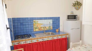 A kitchen with blue tiles, a gas stove, a sink, a microwave, and a refrigerator.