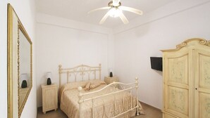 A bedroom with a bed, bedside tables, a wardrobe, a ceiling fan, and a mirror.