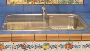 A kitchen with a sink, blue tiles, and a decorative backsplash depicting a beach scene.