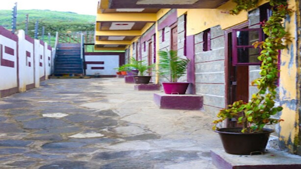 A narrow stone-paved corridor with a yellow building on one side, featuring multiple windows and potted plants. - Garden of Favour Resort (Naivasha)