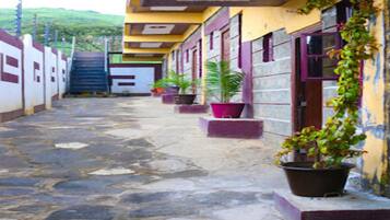 A narrow stone-paved corridor with a yellow building on one side, featuring multiple windows and potted plants.