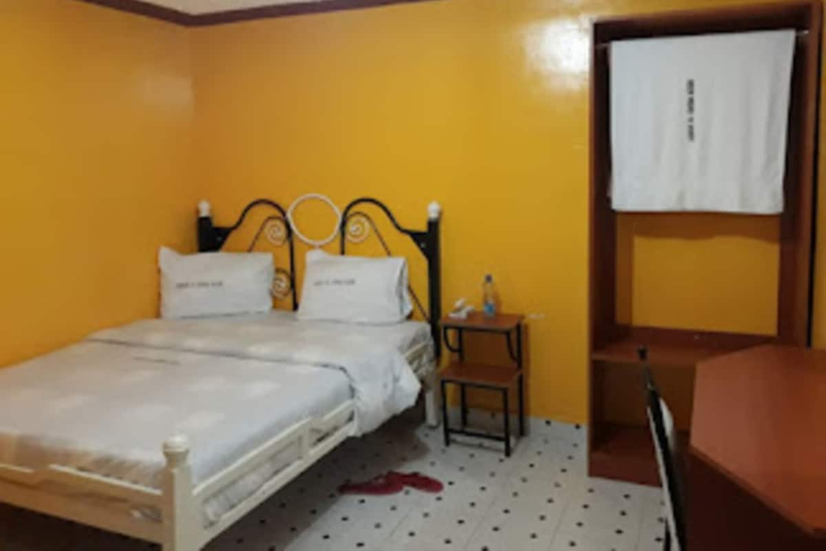 A single-bed room with a wooden headboard, a small bedside table, and a chair.