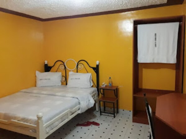 A single-bed room with a wooden headboard, a small bedside table, and a chair.