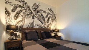 A bedroom with a bed, two bedside tables, and a wall mural of palm leaves.