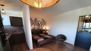 A modern bedroom with a bed, a chair, a dining table with plates and a glass, and a kitchen area with a sink and cabinets.