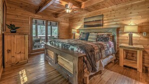 Ein Schlafzimmer einer Holzhütte mit einem Bett, zwei Nachttischen, einem Deckenventilator und einem großen Fenster.