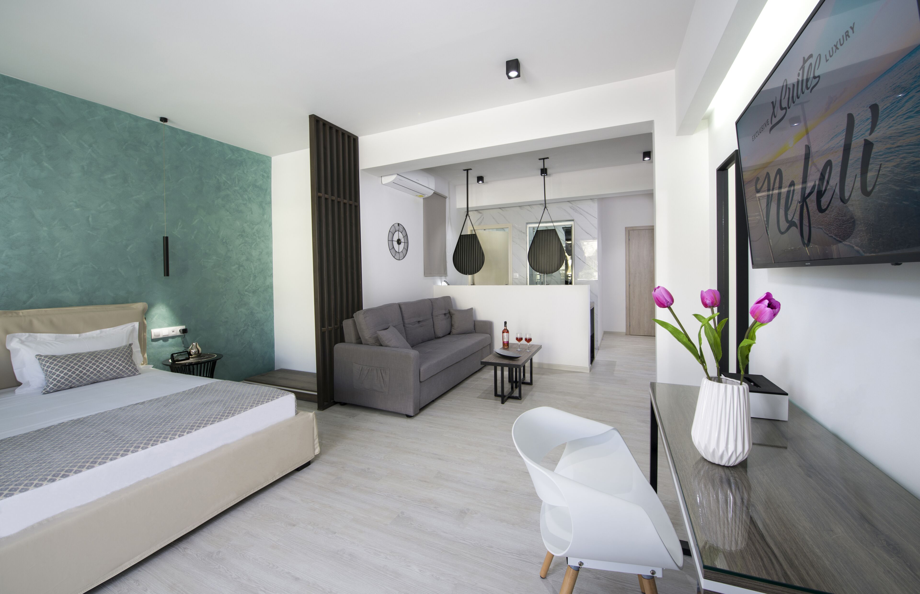 A modern bedroom with a bed, a grey sofa, a small table with a bottle and glasses, and a white chair.