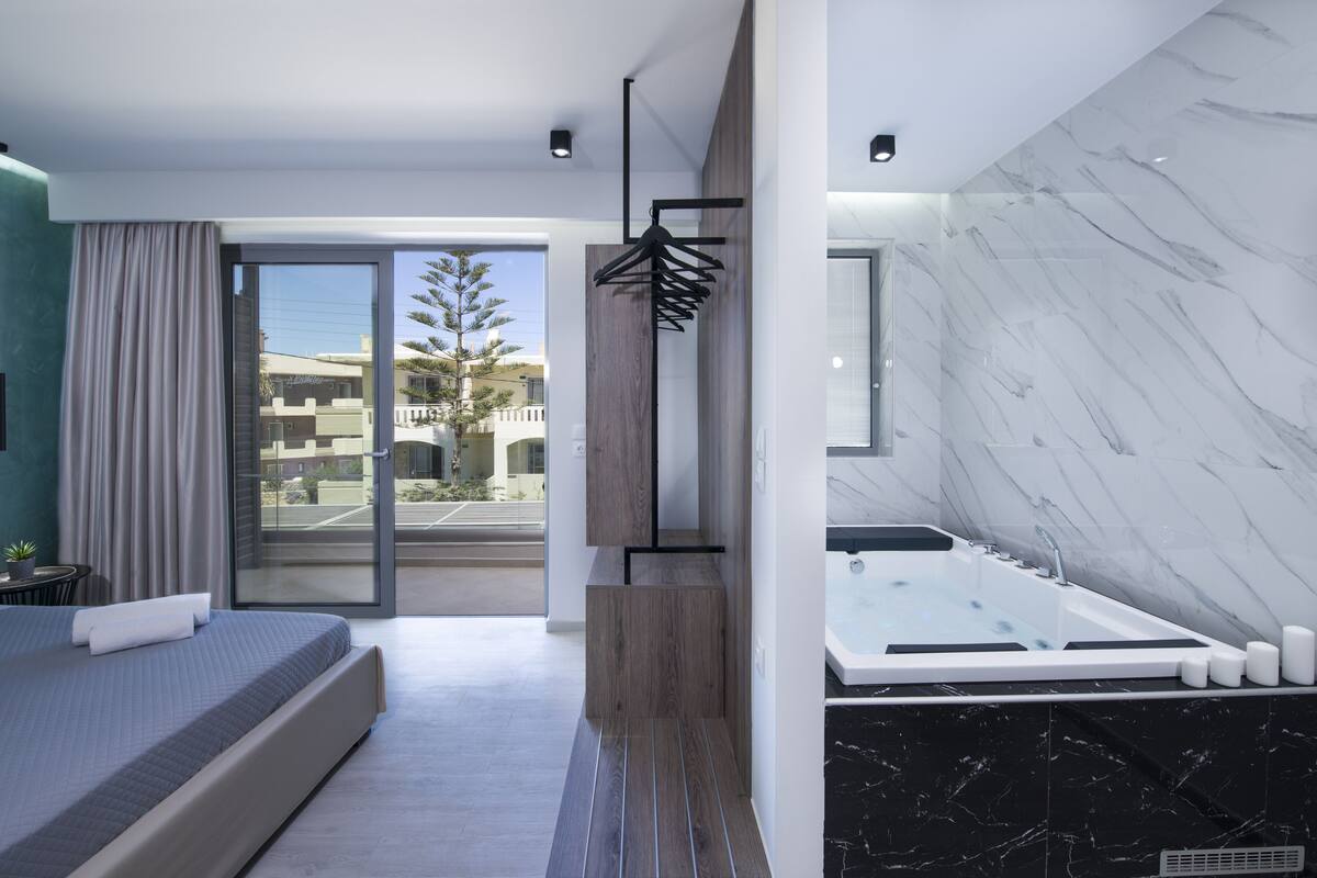 Habitación de hotel moderna con una cama grande, un baño con jacuzzi y vistas al exterior.