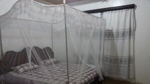 A room with a bed under a mosquito net, a window with patterned curtains, and a plain wall. - Tala Village Inn (Tala)