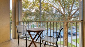 A balcony with a table and two chairs, overlooking a parking area and trees.