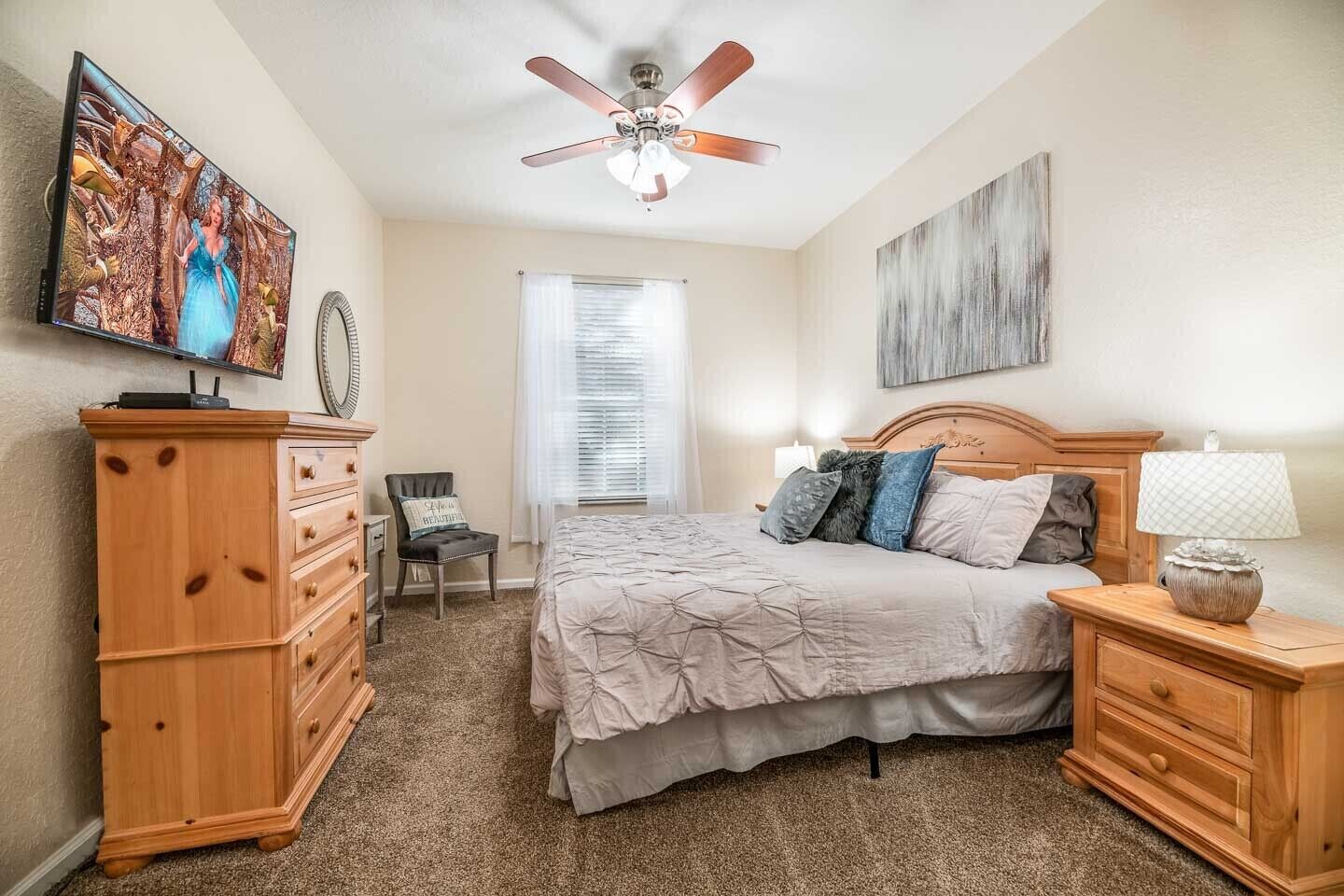 A bedroom with a bed, wooden dresser, chair, and a ceiling fan.