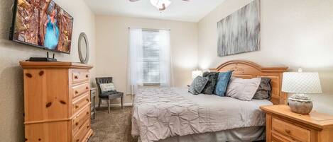 A bedroom with a bed, wooden dresser, chair, and a ceiling fan.