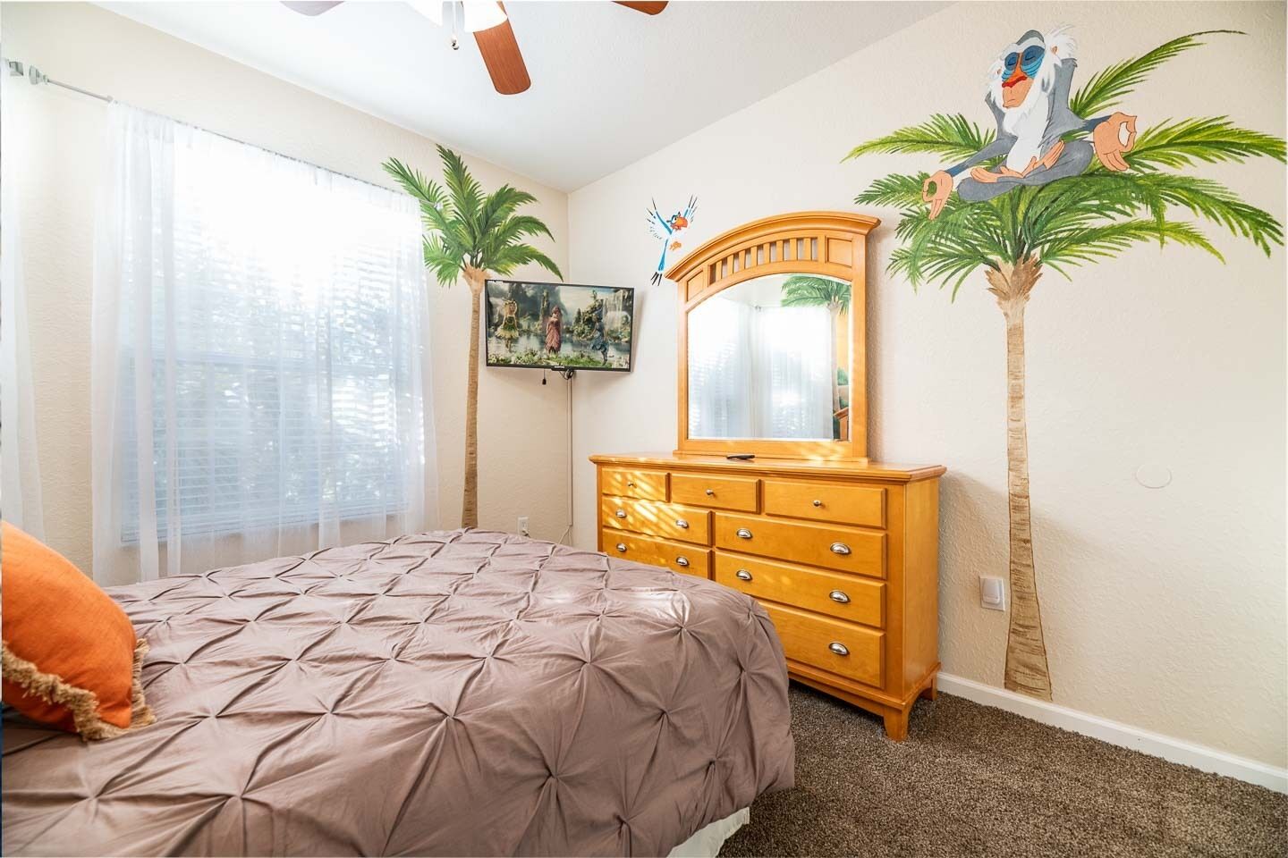 A bedroom with a bed, a dresser, a television, and two palm trees.