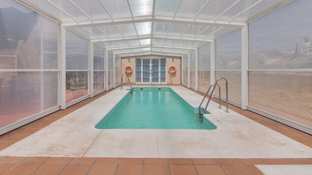 A covered swimming pool with glass walls, a tiled floor, and a clear view of the surrounding area.