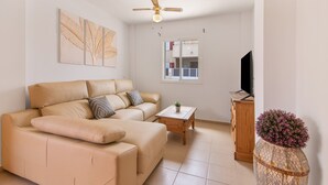 A living room with a sofa, a coffee table, a television, a ceiling fan, and a decorative vase.
