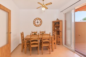A dining area with a wooden table and chairs, a ceiling fan, a wall clock, and a wooden cabinet with shelves. - Holiday Home 'Puerta Marina Costa de la Luz' close to the Sea with Shared Pool (La Redondela (Isla Cristina))