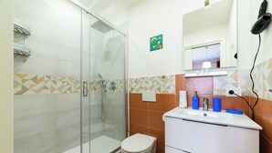 A bathroom with a glass shower enclosure, a toilet, a sink with a mirror above it, and a hairdryer on the wall. - Lovely Bed and Breakfast in Center of Sorrento (Sorrento)