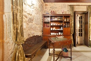 Una habitación con pared de piedra, muebles de madera, un banco, una mesa con superficie de vidrio y una puerta.