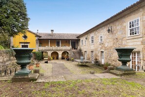 Un patio con un edificio amarillo, muros de piedra y dos grandes macetas verdes.