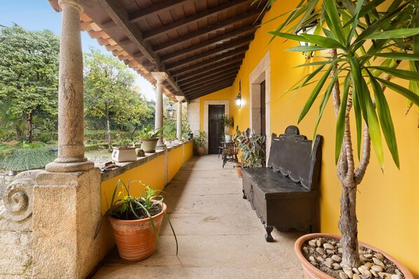 A covered outdoor area with a bench, potted plants, and a stone pillar.