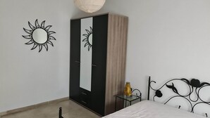 Ein Schlafzimmer mit Bett, Kleiderschrank, einem kleinen Tisch mit Lampe und einem Wandspiegel.