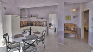 A dining area with a round table and chairs, a kitchen in the background, and a wooden bench in the adjacent room. - Apartment with breakfast - Only Adults (Tignale)