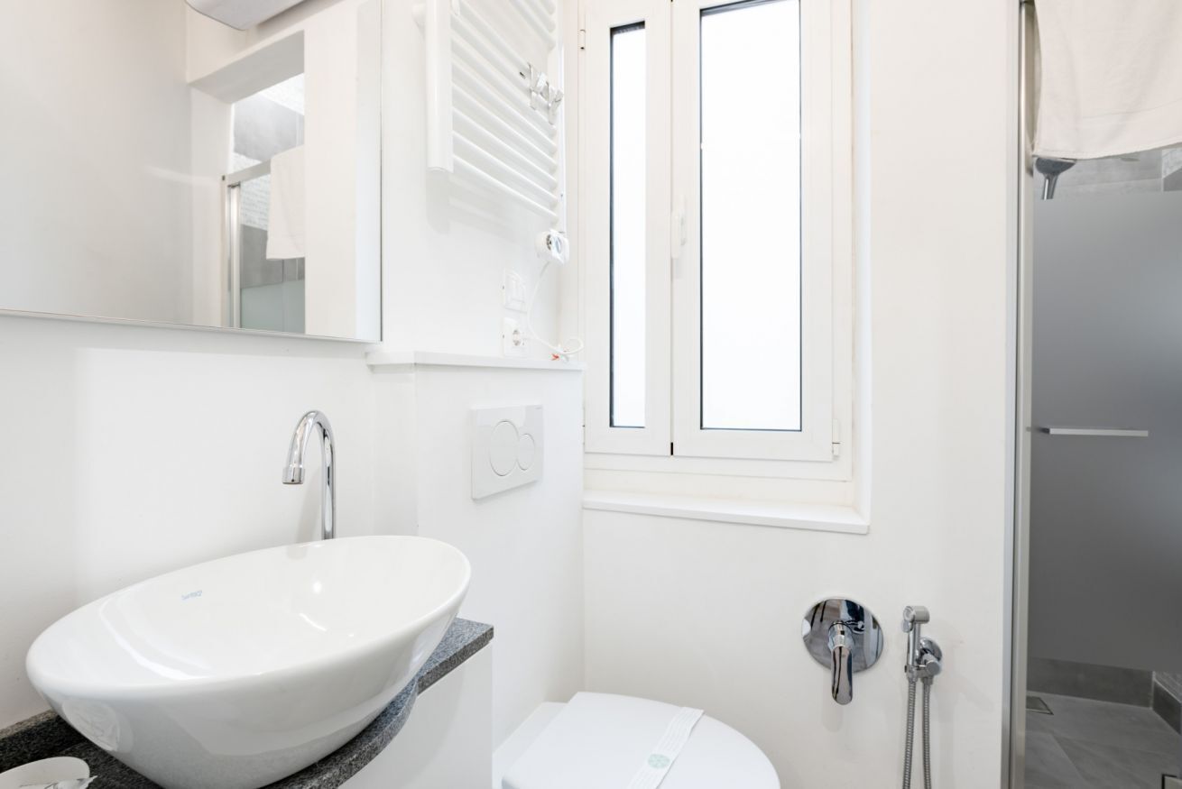 Une salle de bain avec un lavabo blanc, des toilettes, une douche et une fenêtre.