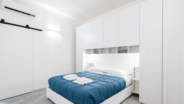 A modern bedroom with a bed, white wardrobe, and built-in shelves. - GuestHost - Bright and functional 35 sqm apartment, able to accommodate up to 2 people, located on the first floor (without elevator) of a building within Gioberti district. The property is located in a lively neighborhood, full of services and well serv (Firenze)
