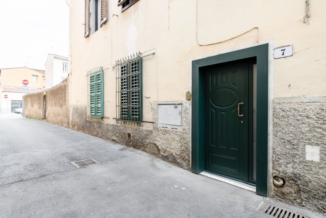 Un bâtiment avec une porte verte, une enseigne portant le chiffre « 7 », et une rue où l’on aperçoit, au loin, un panneau de signalisation indiquant « STOP ».