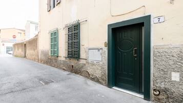 Un bâtiment avec une porte verte, une enseigne portant le chiffre « 7 », et une rue où l’on aperçoit, au loin, un panneau de signalisation indiquant « STOP ».