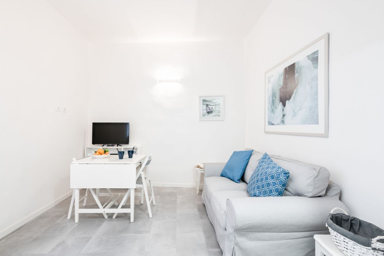 Un salon moderne avec un canapé gris, un meuble TV blanc et un tableau encadré accroché au mur.