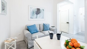 A modern living room with a grey sofa, a coffee table, a framed abstract painting, and a door leading to another room. - GuestHost - Bright and functional 35 sqm apartment, able to accommodate up to 2 people, located on the first floor (without elevator) of a building within Gioberti district. The property is located in a lively neighborhood, full of services and well serv (Firenze)