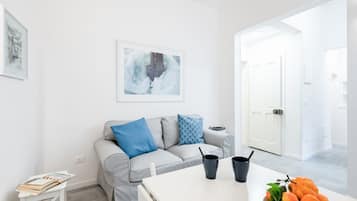 Un salon moderne avec un canapé gris, une table basse, un tableau abstrait encadré et une porte donnant sur une autre pièce.