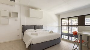 Een moderne slaapkamer met een bed, een bureau en een raam met uitzicht op gebouwen.