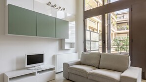Een moderne woonkamer met een witte tv-meubel, een beige bank en een groene kast.