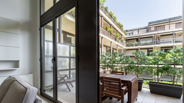 Een modern appartement met een schuifdeur naar een terras buiten, met een eettafel en stoelen.