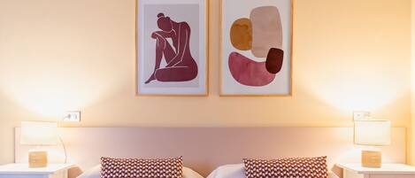 A hotel room with a bed, two nightstands, two lamps, two pillows, and two framed artworks on the wall.
