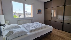 Une chambre à coucher avec un lit, une fenêtre, un radiateur, une table de chevet, une lampe, une armoire et un tableau accroché au mur.