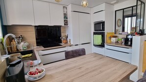 Une cuisine moderne avec des meubles blancs, une table à manger en bois et un four encastré.