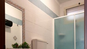 Un baño con lavamanos, dos inodoros, ducha y espejo con azulejos decorativos.
