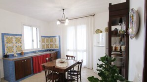 Una cocina con una mesa de comedor, sillas, una cortina roja y una planta en maceta.