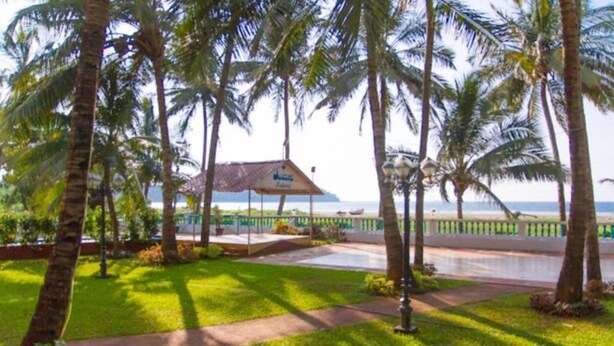 Un jardín tropical con palmeras, un pabellón y vista al océano.