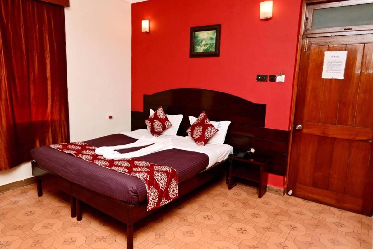 Ein Hotelzimmer mit einem großen Bett, einem Holzkopfteil, einem Nachttisch, einer roten Wand und einer Tür.