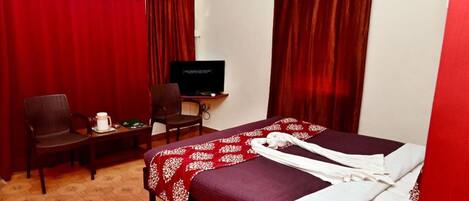 Habitación de hotel con cama, escritorio con televisor, dos sillas y una mesa pequeña con una taza y un objeto verde.