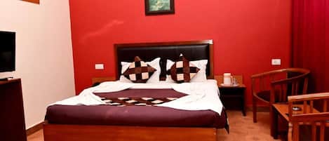 A hotel room with a large bed, a TV, a wooden desk, and a dining area.