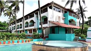 Un hotel de dos pisos con piscina, zona de estar al aire libre y palmeras.
